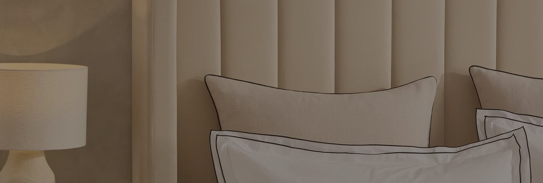 Cream panelled headboard with pillows and a bedside lamp